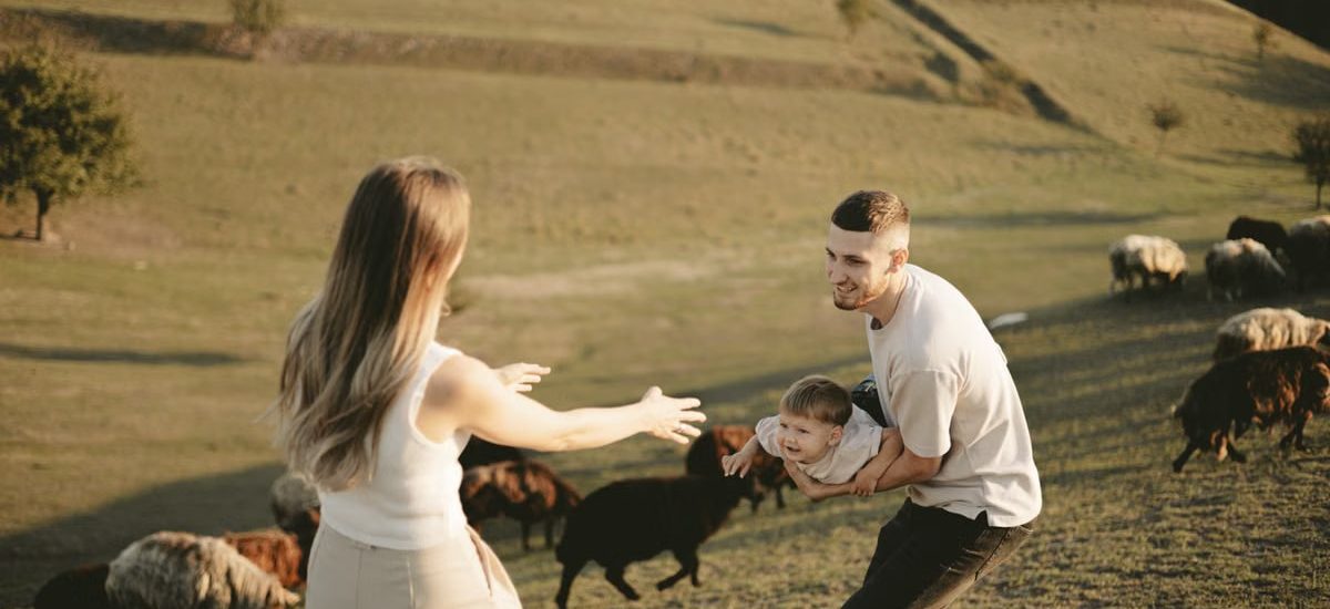 A joyful family with a child in a pastoral setting, embracing countryside life with grazing sheep.