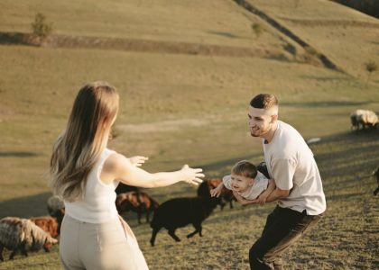 A joyful family with a child in a pastoral setting, embracing countryside life with grazing sheep.